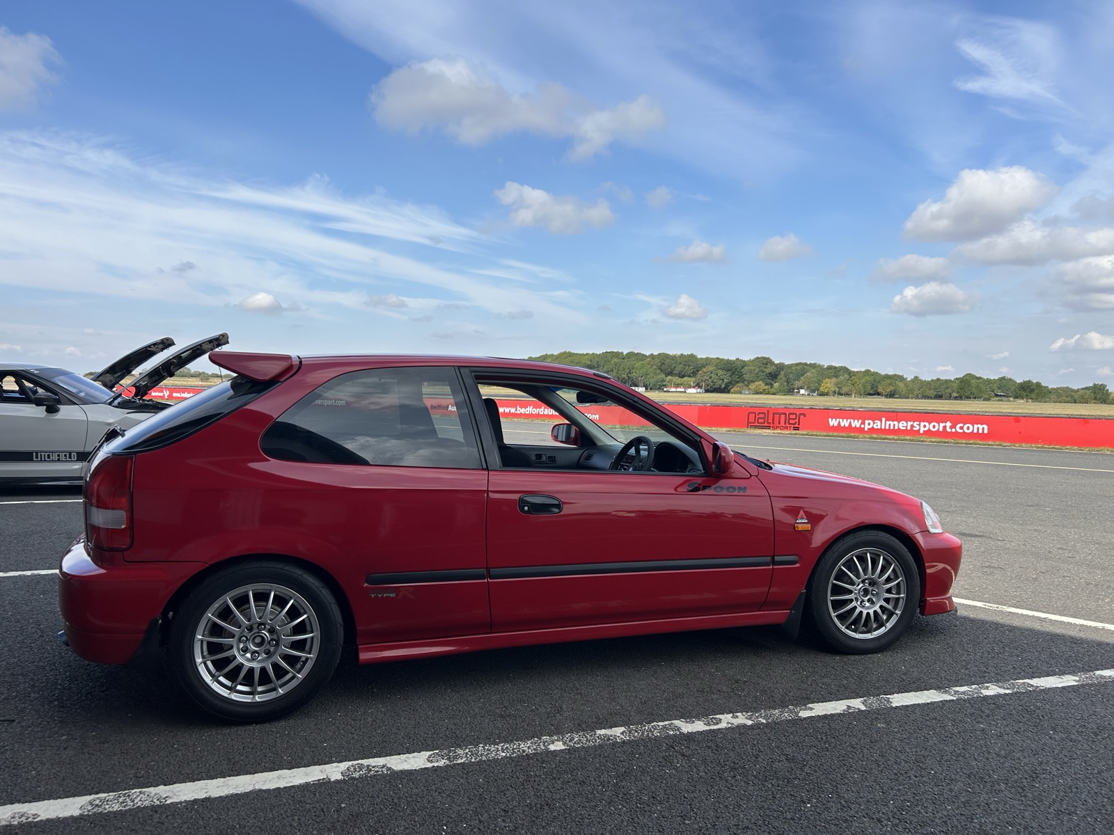 The red Civic EK on track at Bedford Autodrome, side profile, blue sky in the background